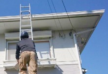 はしごに登り家を見る作業員