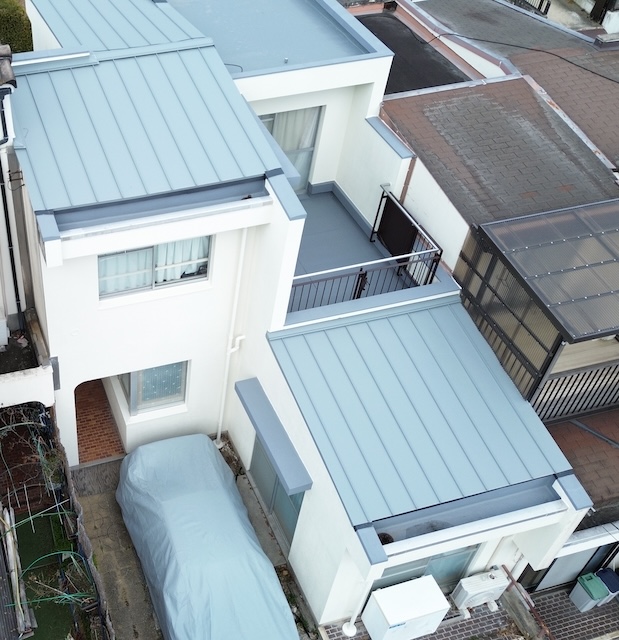 大阪府茨木市での屋根シングル葺き、外壁塗装、ベランダ防水工事完了後のドローン空撮写真。街の屋根やさん八尾店による施工。「数値と可視化」に基づく提案で実現した美しい仕上がり