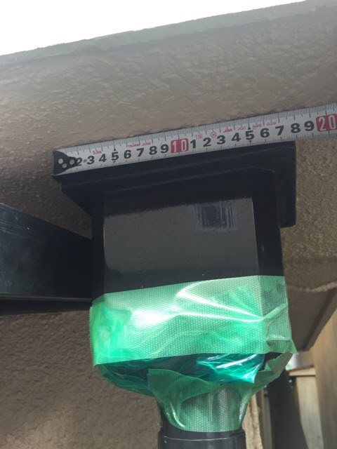 ベランダ下の集水器（四角い箱）のサイズを約15センチと計測している様子