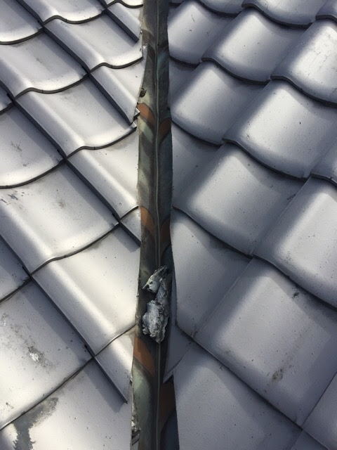 東大阪市の屋根雨漏り調査。谷樋（たにとい）の銅板が変色し、剥がれた漆喰の塊が詰まっている危険な状態。