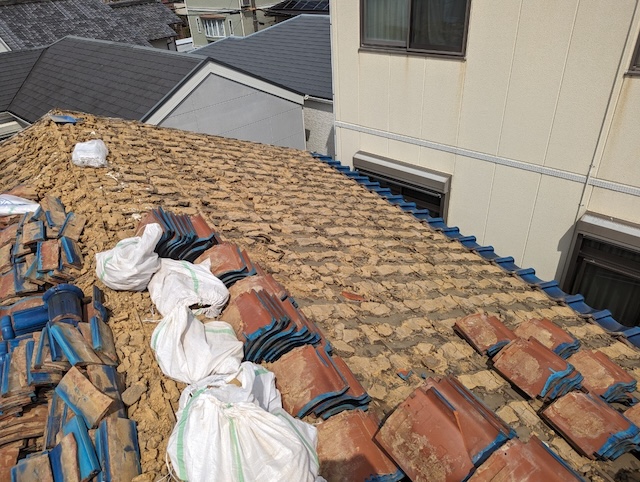 屋根の軽量化のため職人が大量の葺き土を撤去している解体作業の様子
