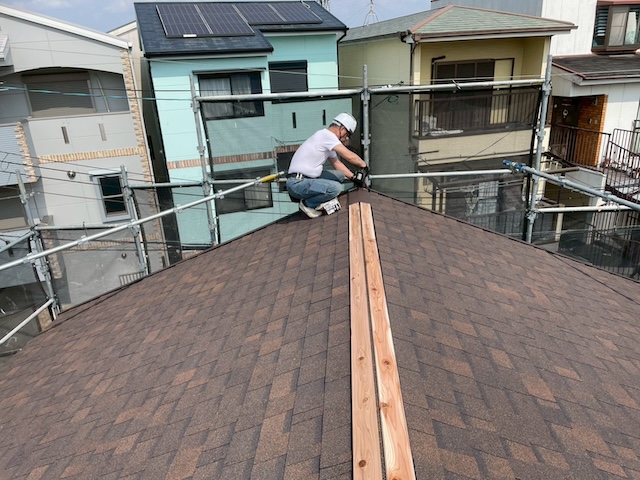 葺き替え工事の最終工程。屋根の頂点にあたる棟（むね）部分に防腐処理を施した木材（貫板）を固定する職人。