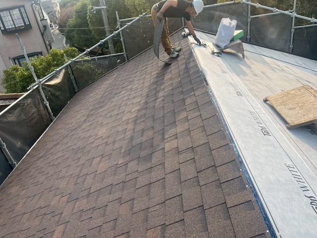 新しい防水シートの上から、軽量屋根材「ニチハ アルマ」を一枚ずつ専用の接着剤と釘で確実に固定する施工風景。