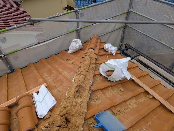 屋根の軽量化のために古い葺き土を土嚢袋に詰めて撤去する作業